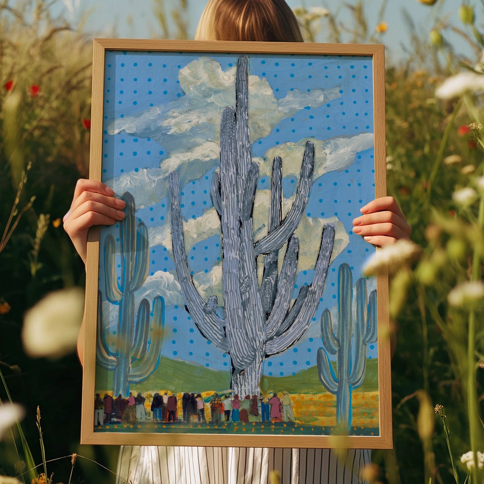 Person holding a framed artwork of cacti in a field